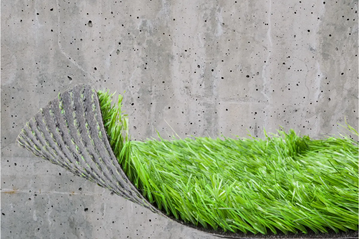 Obraz prezentuje sztuczną trawę na tle betonowej powierzchni.